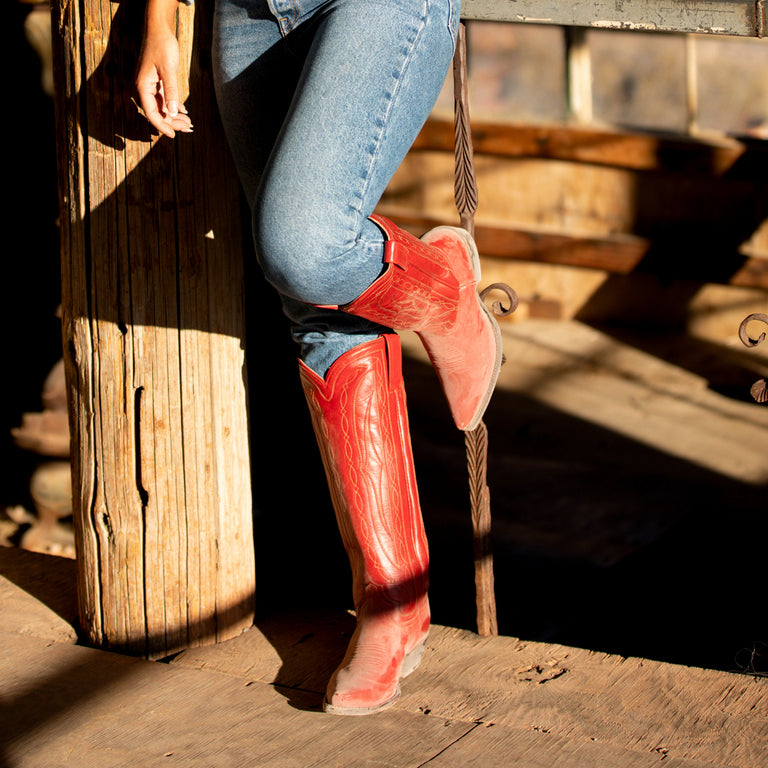 Person wearing red cowboy boots and blue jeans standing on wooden steps.