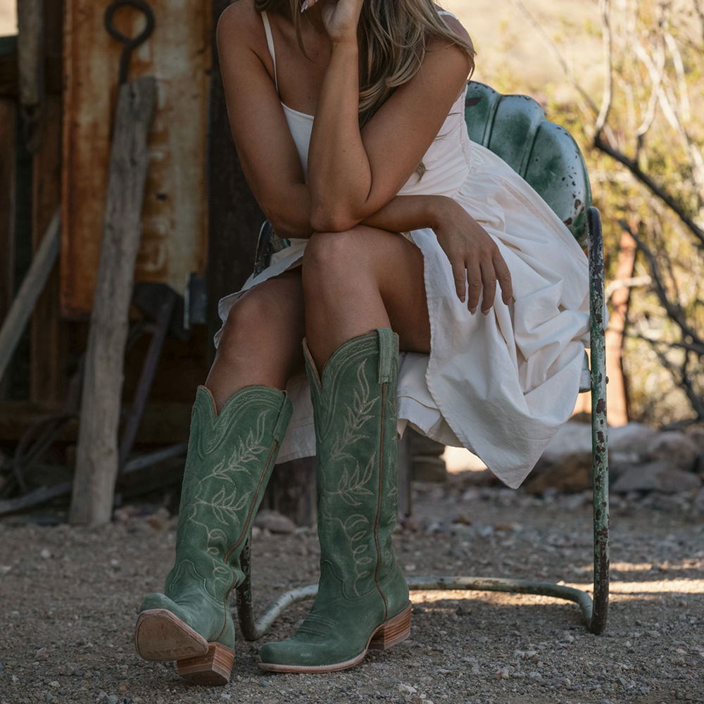 Woman wearing green cowboy boots sitting on a chair outdoors.