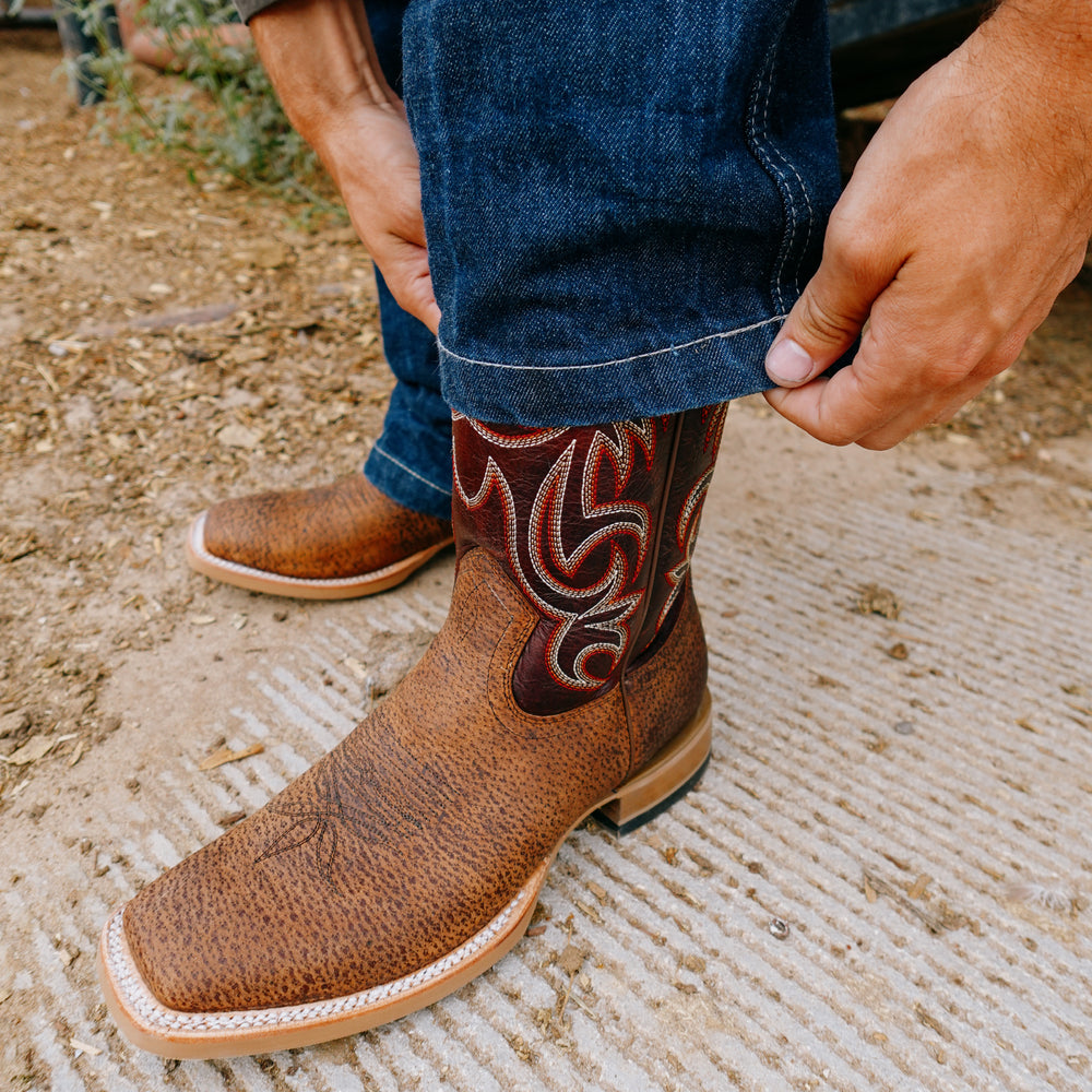 Brown cowboy boot with intricate design on a textured surface