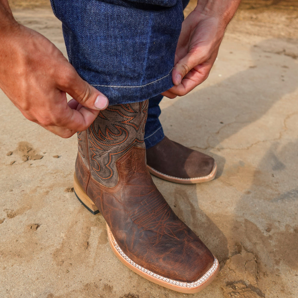 Brown leather cowboy boot with intricate patterns on a stone surface