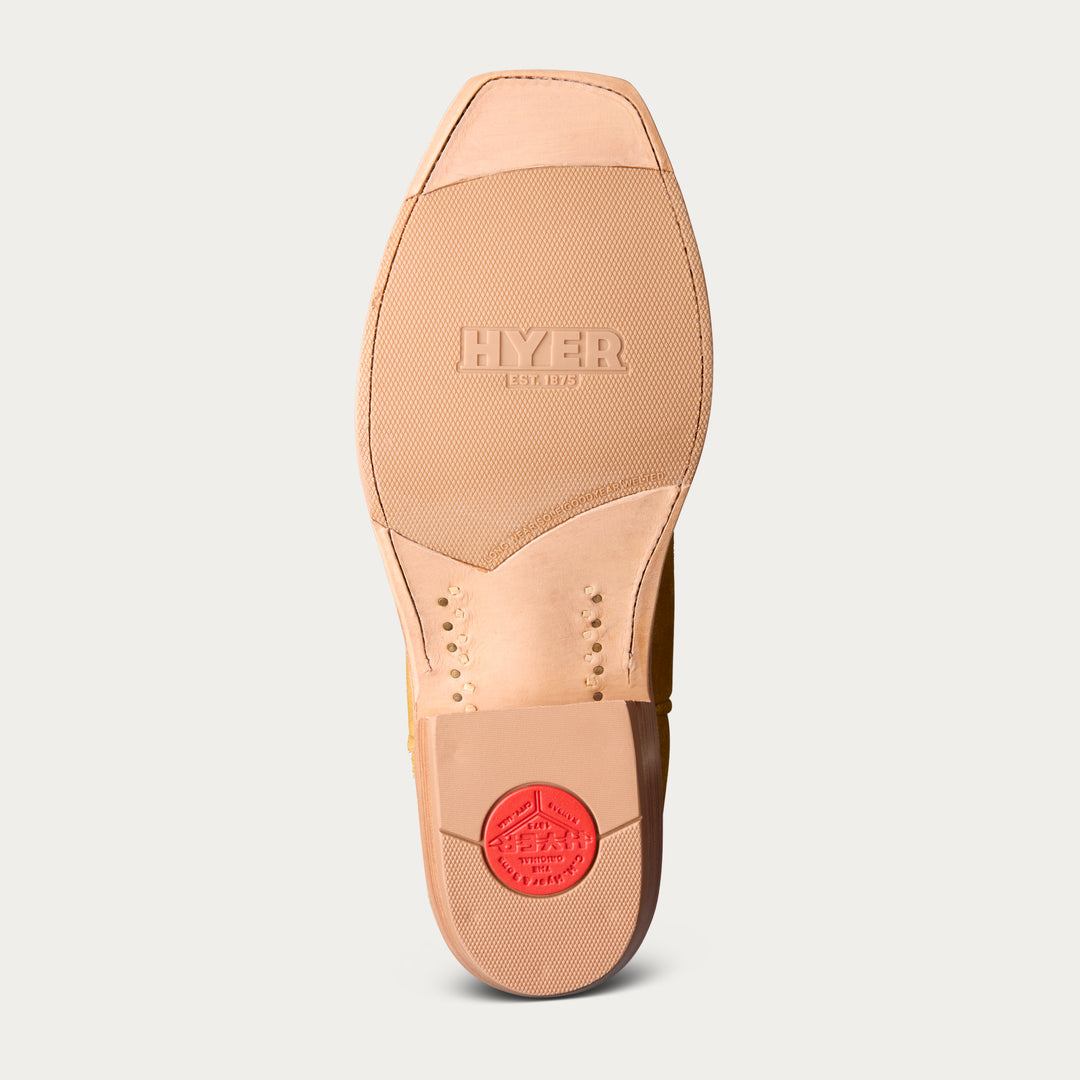 The outsole of a light tan leather boot or shoe, showing the brand name 'HYER' embossed on the forefoot and a red circular heel patch, set against a light gray background.