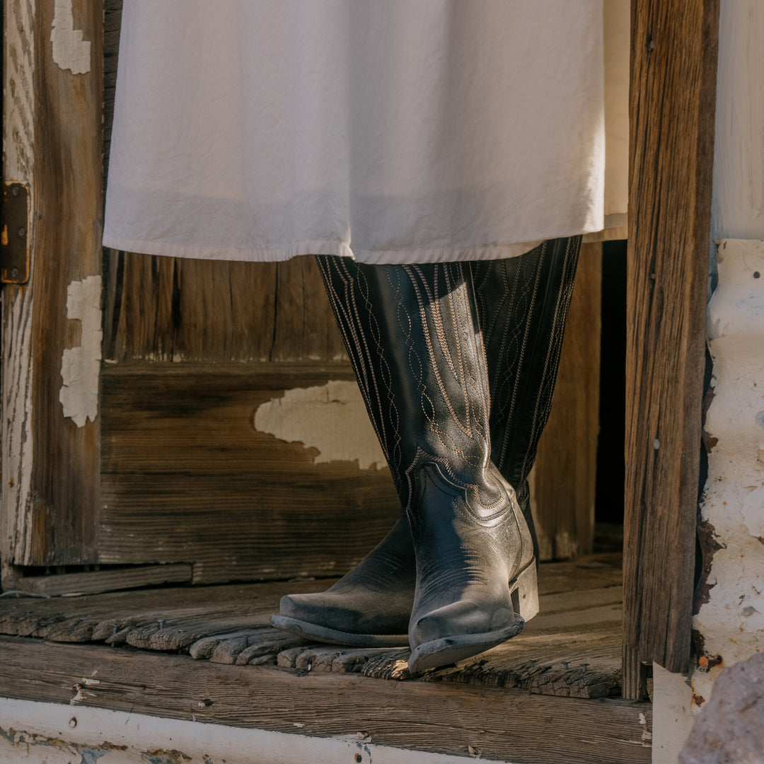 Person wearing a white dress and black boots stepping onto a wooden platform.