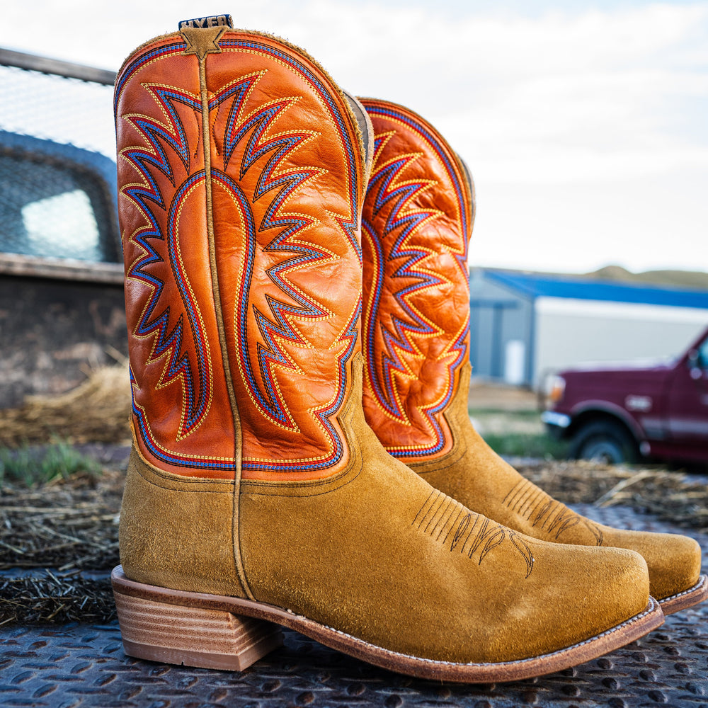 Pair of tan and orange cowboy boots with intricate designs on a metal surface.