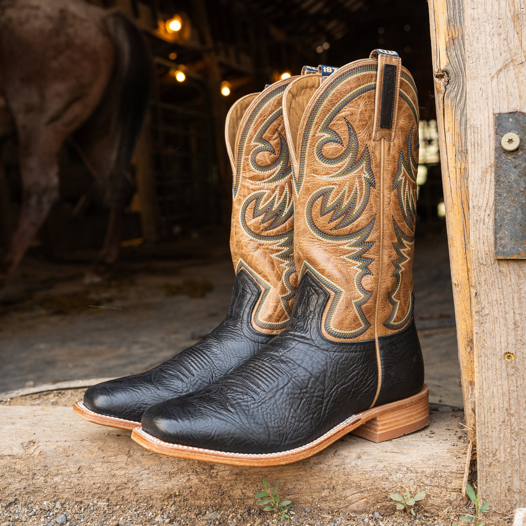 Pair of cowboy boots with intricate designs on a wooden surface in a rustic setting.