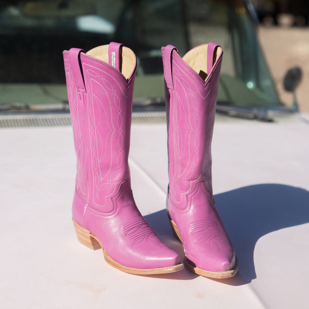 Pair of pink cowboy boots on a white surface with a blurred background