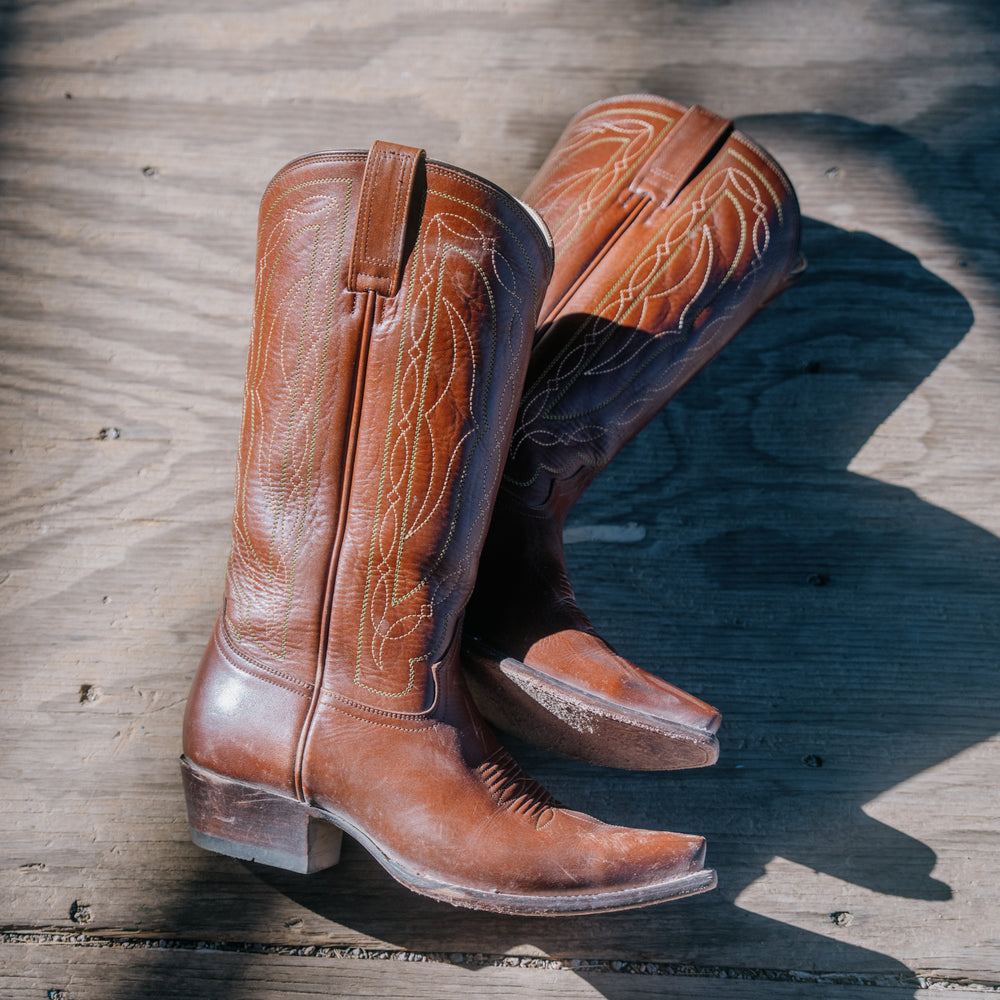 Pair of brown leather cowboy boots on a wooden surface