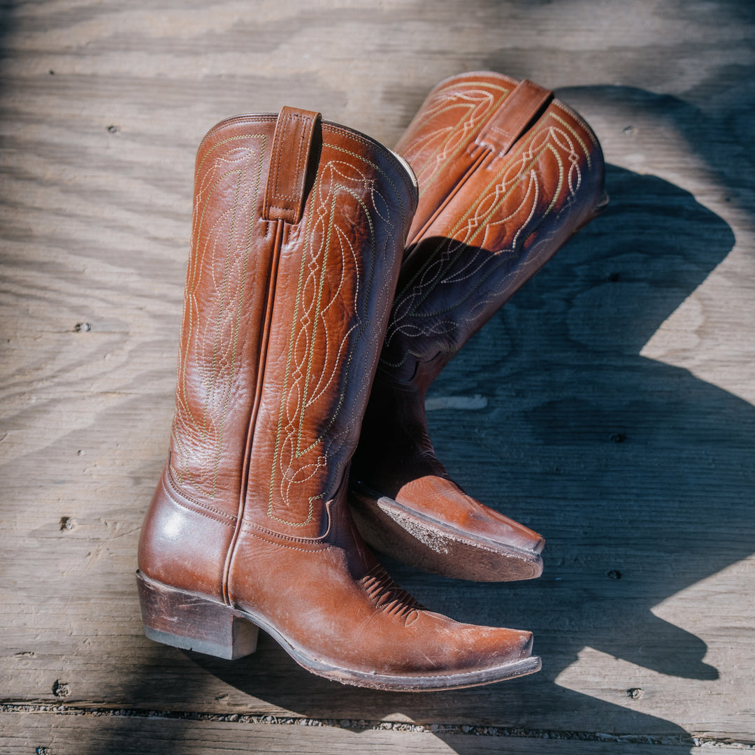 Pair of brown leather cowboy boots on a wooden surface