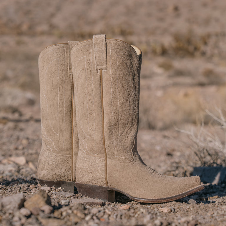 Pair of beige cowboy boots on a dirt ground with a blurred natural background