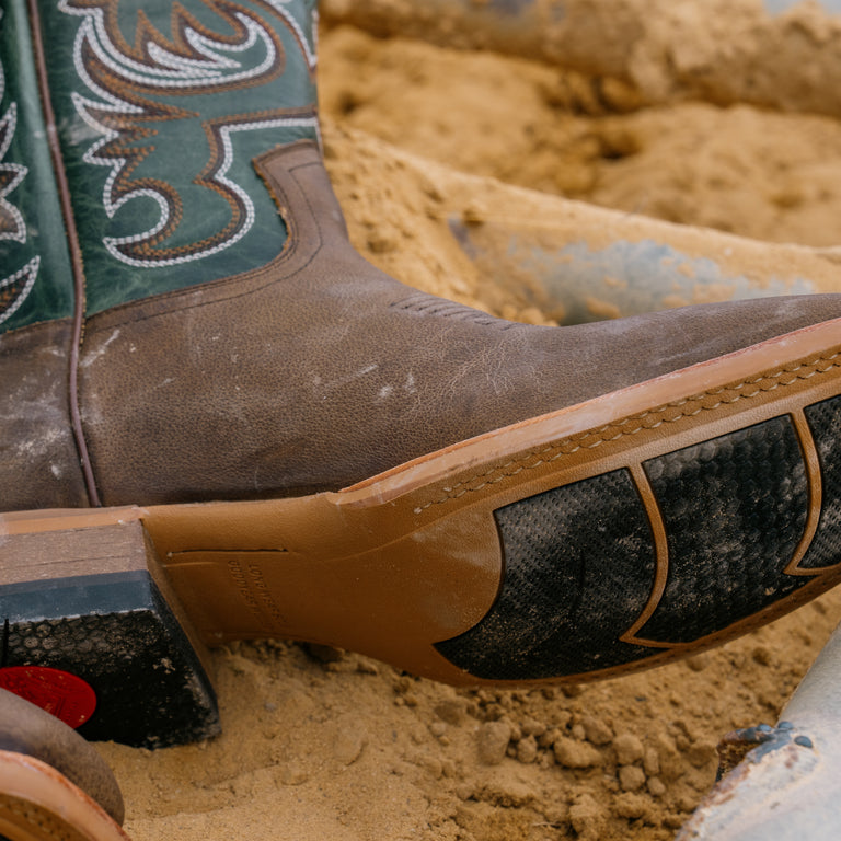 Close-up of a worn cowboy boot with detailed stitching on a sandy background