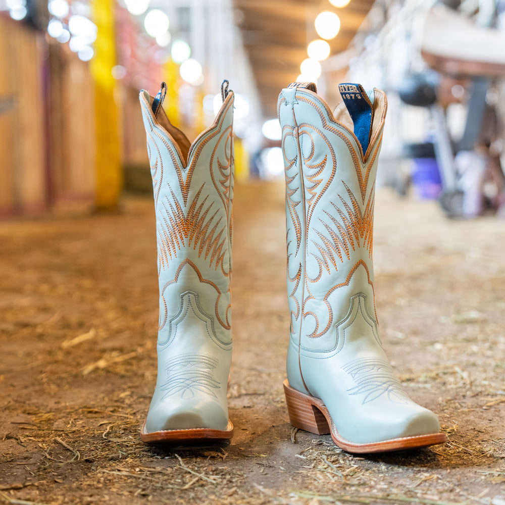 Pair of light blue cowboy boots with brown accents on a wooden floor.