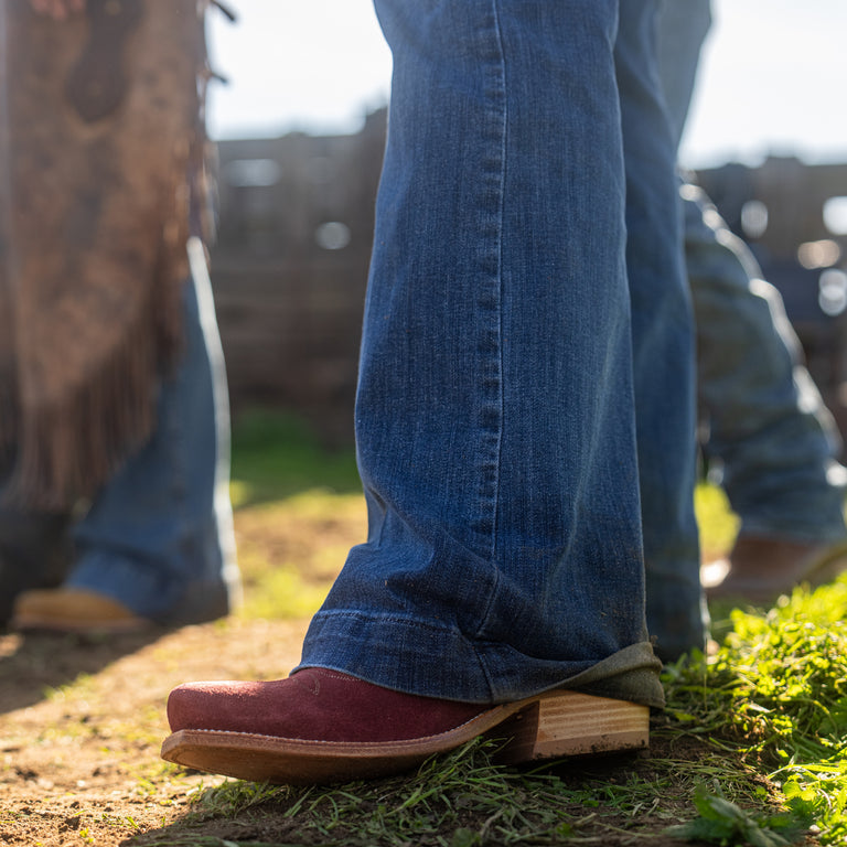 Close-up of a person wearing blue jeans and red cowboy boots standing on grass 