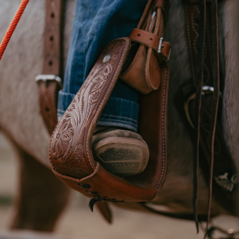 Photo of cowboy boot toe in stirrup with blurred close up of horse in background