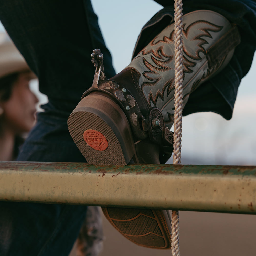 Sole of cowboy boot resting on metal bar with cowboy boot upper in background