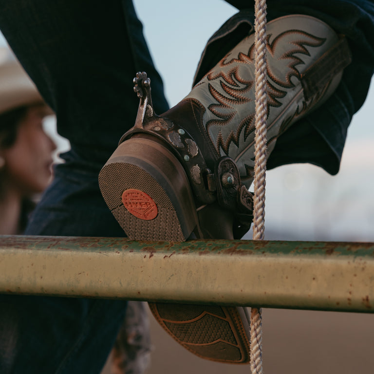Sole of cowboy boot resting on metal bar with cowboy boot upper in background