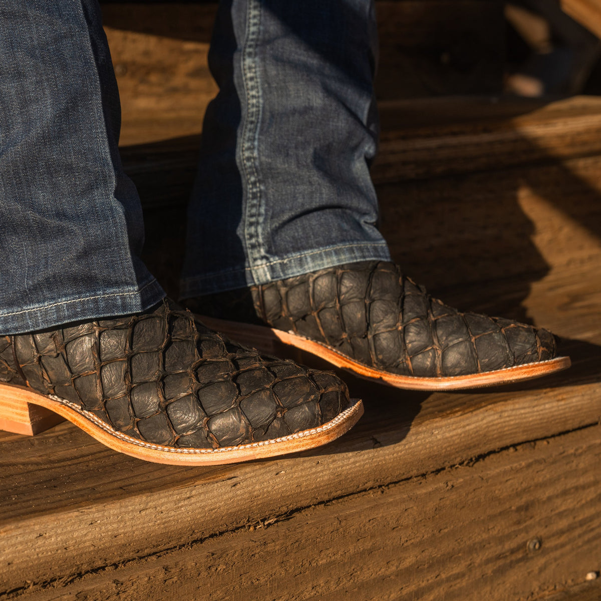 Close up detail of big bass scaled vamp of a pair of cowboy boots resting on wooden stairs