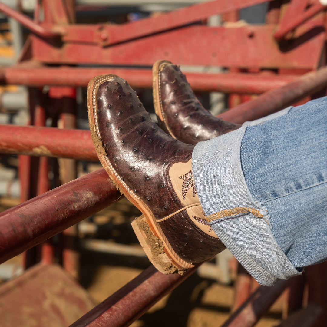 Dark purple leather cowboy boots and blue jeans on a red metal structure
