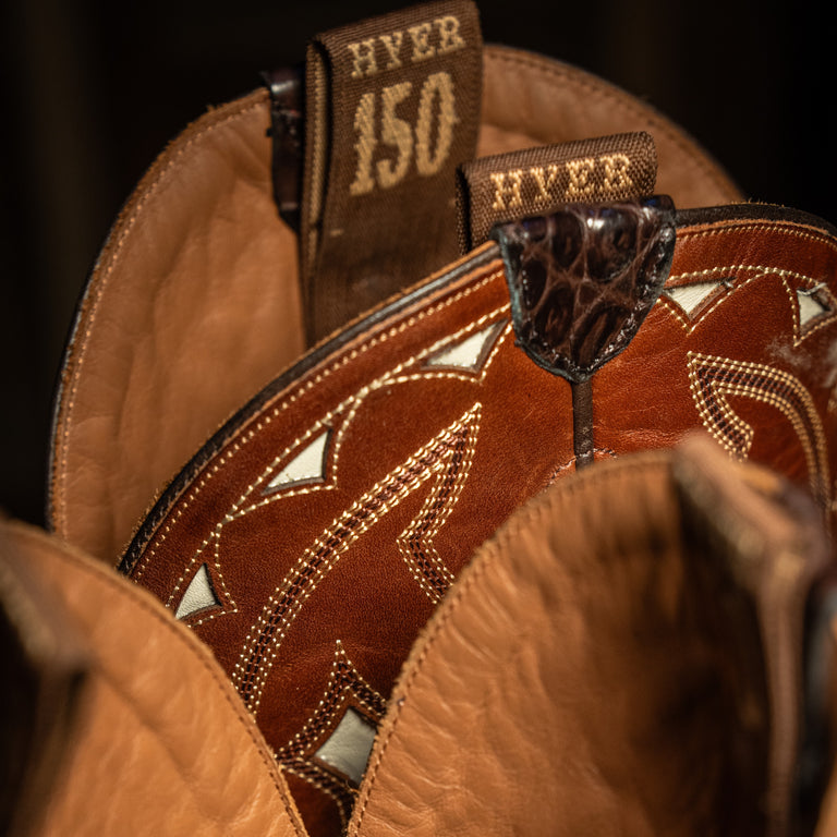 Close-up of a upper edge of cowboy boot pull straps with intricate stitching and 'HYER' branding