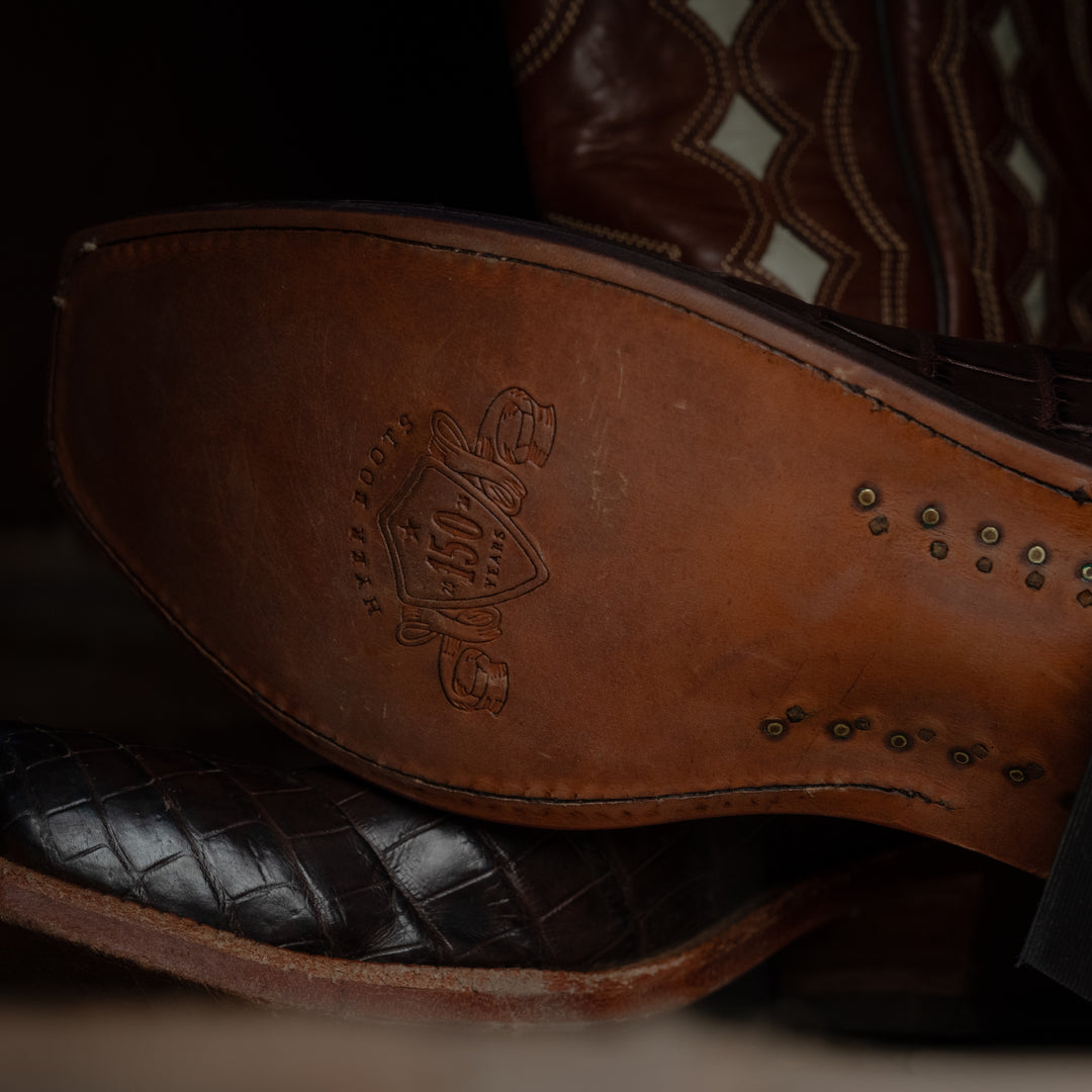 Close-up of a brown leather sole of cowboy boot with a brand logo on a dark background
