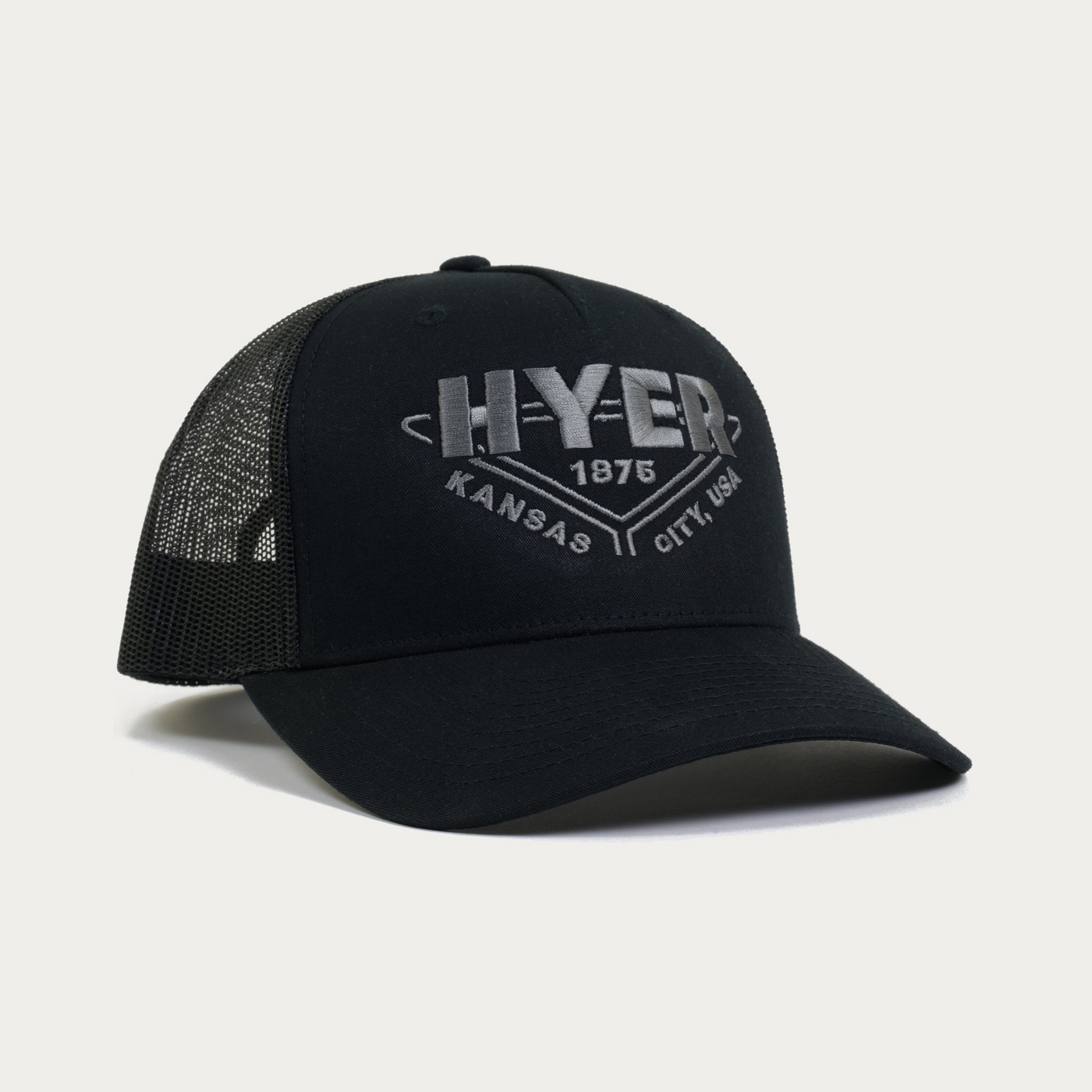 A black trucker-style cap with a curved brim, black mesh back, and a gray embroidered graphic on the front reading 'HYER 1875 KANSAS CITY, USA.'.