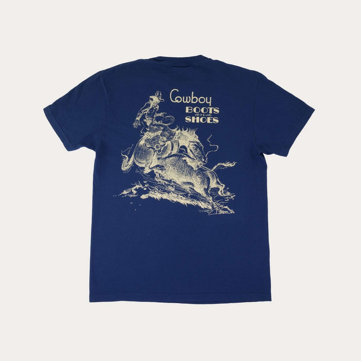 A navy blue short-sleeve t-shirt with a vintage-style cream graphic of a cowboy riding a bucking horse, featuring the text 'Cowboy Boots and Shoes' above it, displayed flat against a light off-white background.