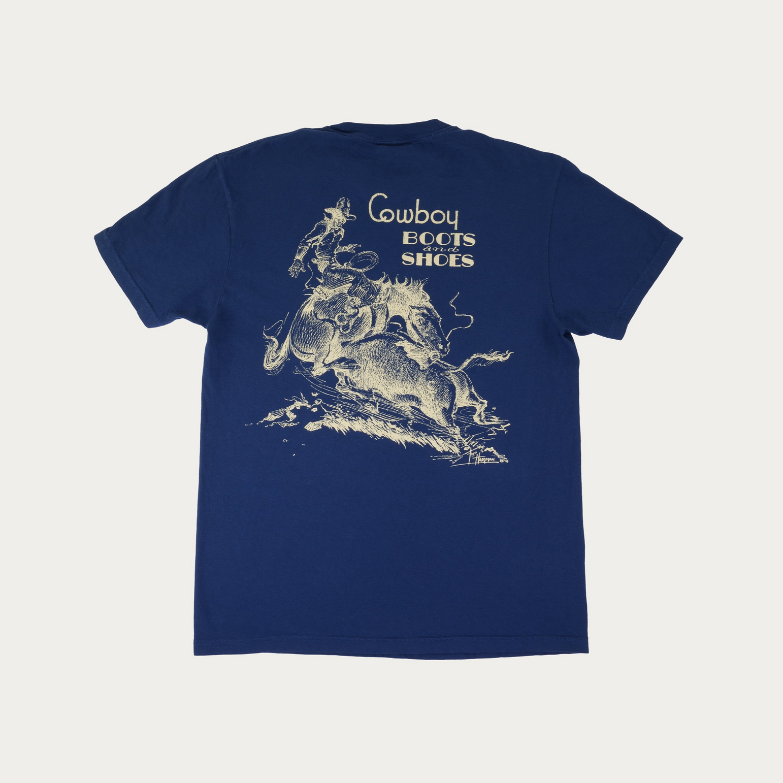 A navy blue short-sleeve t-shirt with a vintage-style cream graphic of a cowboy riding a bucking horse, featuring the text 'Cowboy Boots and Shoes' above it, displayed flat against a light off-white background.