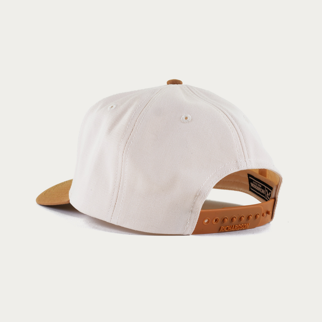 A structured baseball cap shown from a rear three-quarter angle on a clean, light off-white background. The cap features an off-white crown, a tan leather visor, and a tan plastic adjustable back strap.