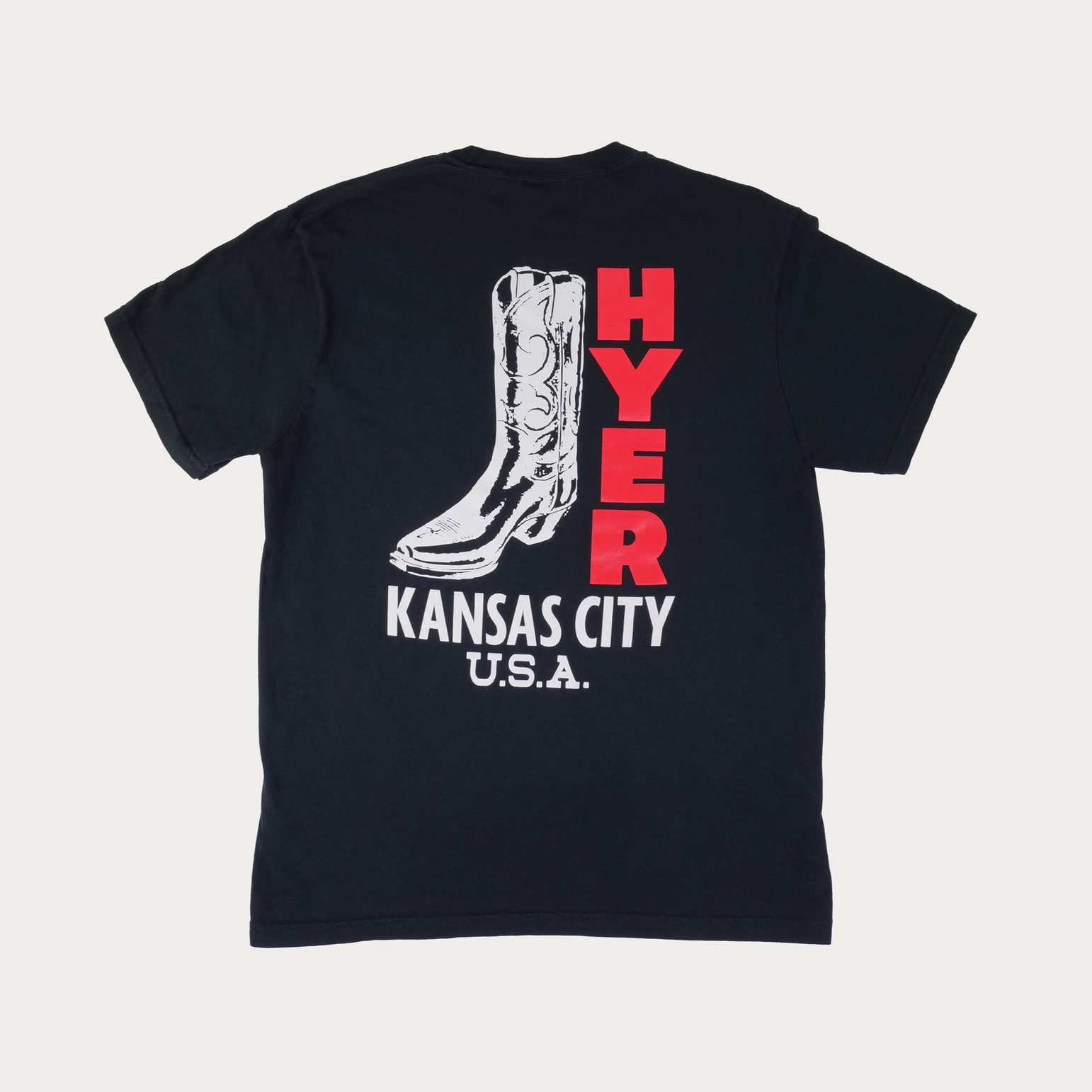 A black short-sleeve t-shirt laid flat against a light gray background, featuring a graphic print on the back with a white cowboy boot, the word 'HYER' in red, and 'KANSAS CITY USA' in white.