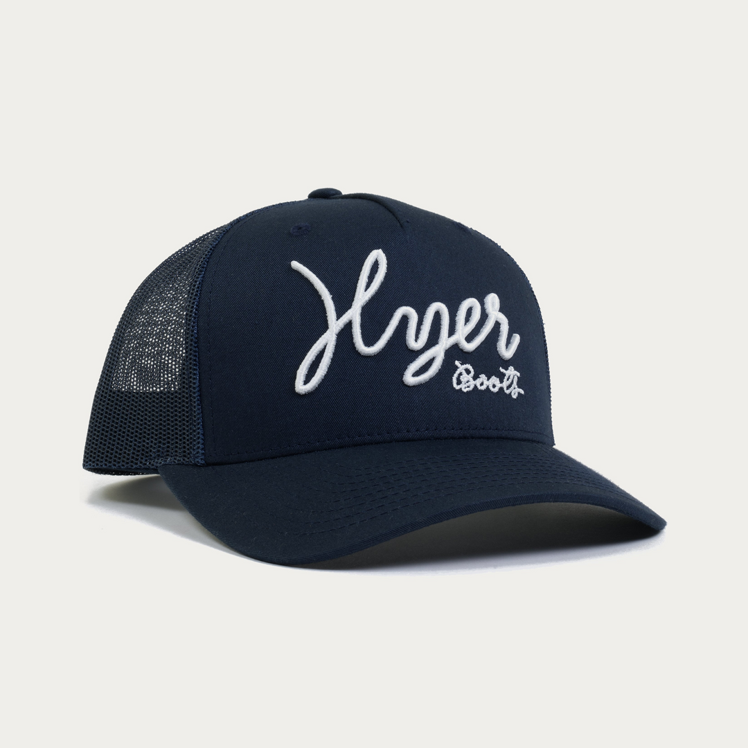 Dark navy blue trucker cap with HYER BOOTS script text in white on an off white background