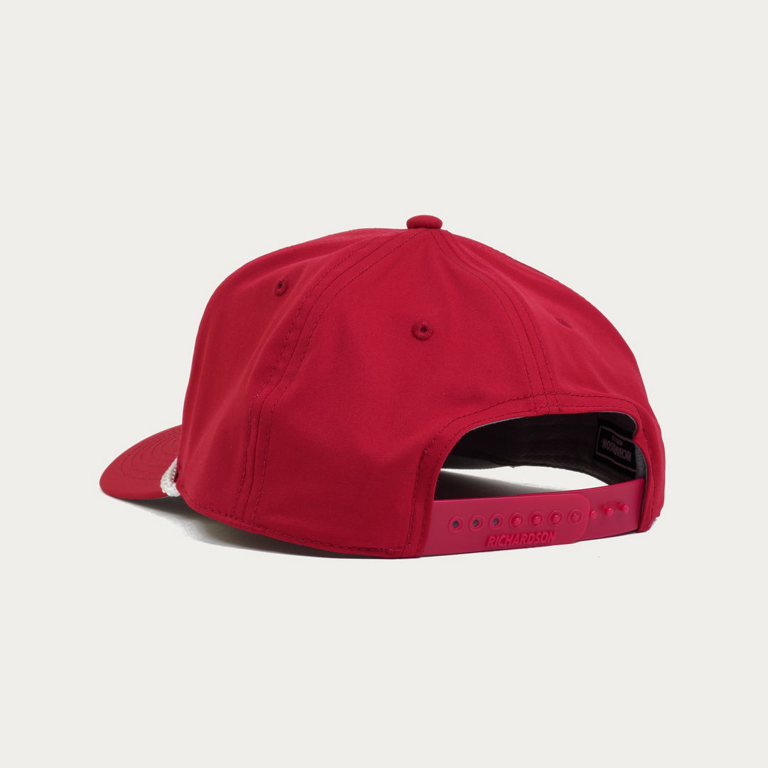 A red snapback cap shown from the back, featuring a structured six-panel crown, a curved brim, and an adjustable hook-and-loop strap with a red plastic buckle, photographed on a light gray background.