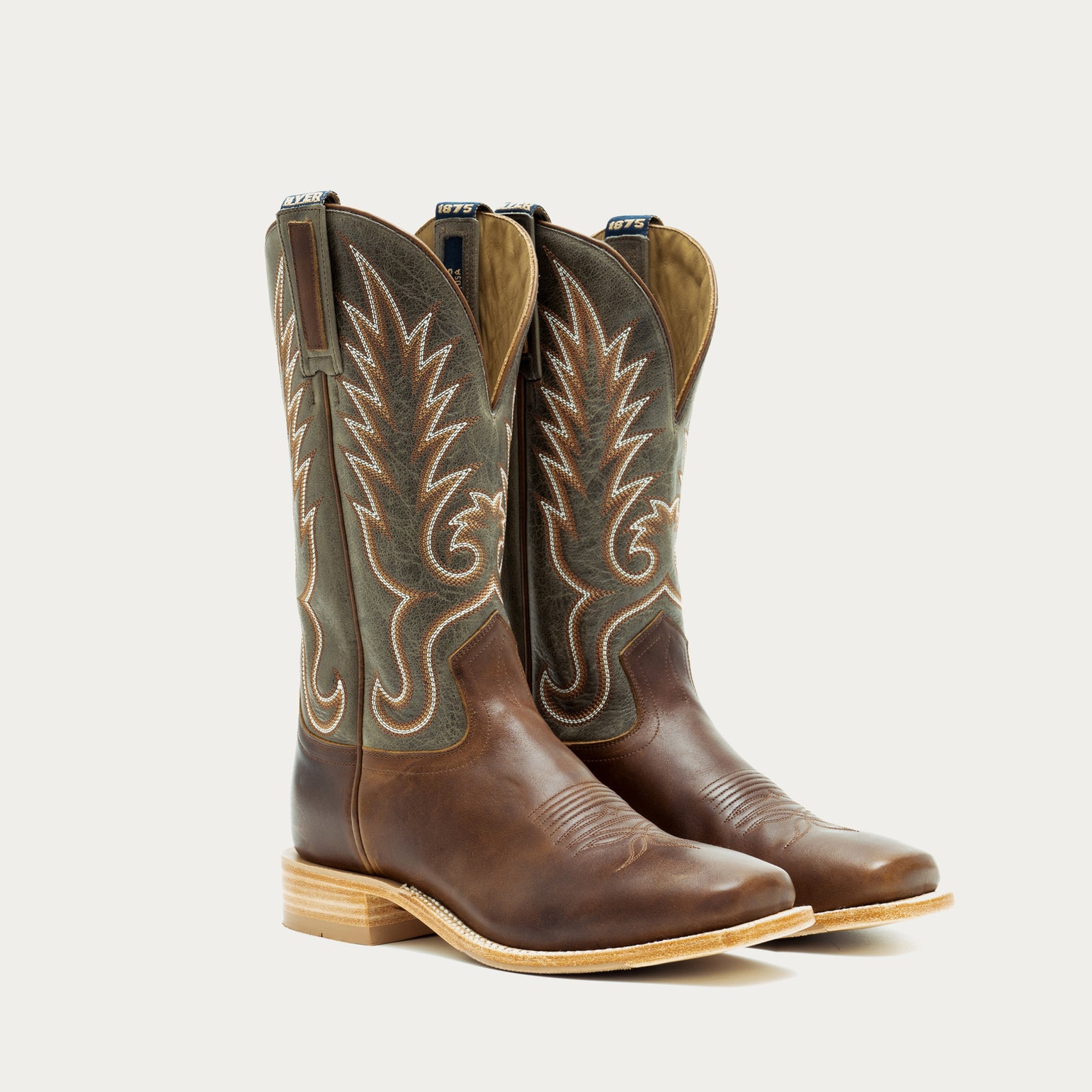 Pair of brown and green cowboy boots with intricate designs on a light gray background