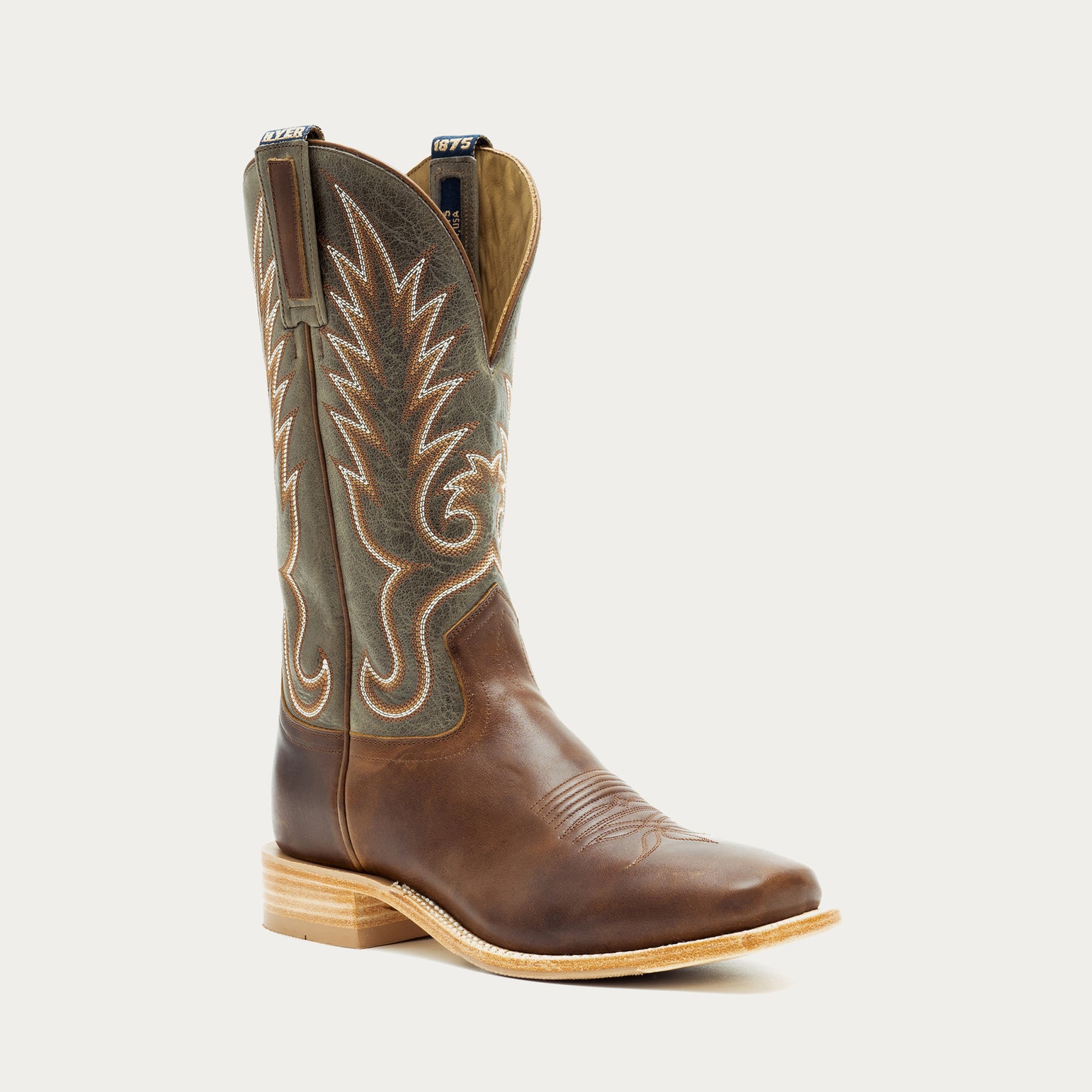Brown and green cowboy boot with intricate white stitching on a light gray background