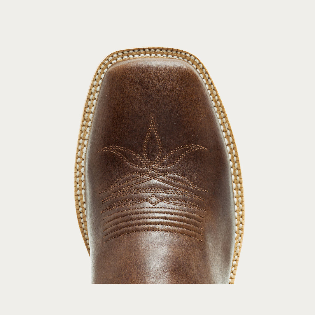 Close-up of a brown leather boot with intricate stitching on a light gray background