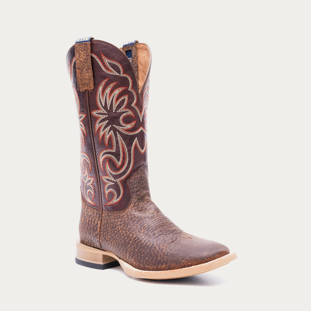 Brown cowboy boot with white and red intricate stitching on a light gray background