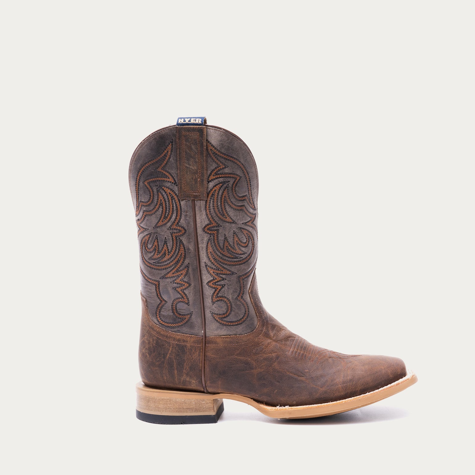 Brown cowboy boot with tan and black intricate stitching on a light gray background