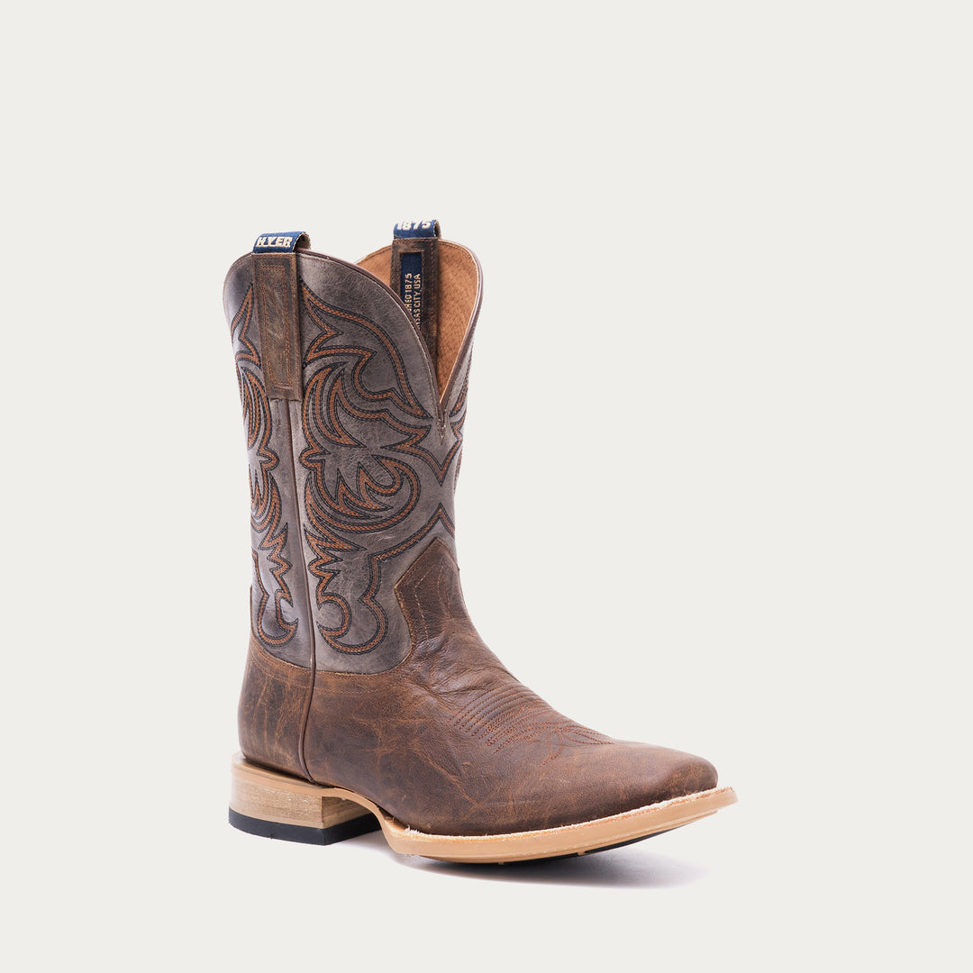 Brown cowboy boot with tan and black intricate stitching on a light gray background