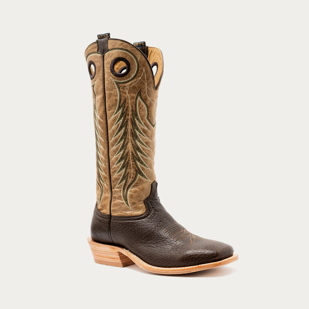 A single tall western cowboy boot shown in side profile on a light gray studio background. The shaft is tan with dark brown embroidered feather-like detailing, while the lower vamp and pull tabs are dark brown.
