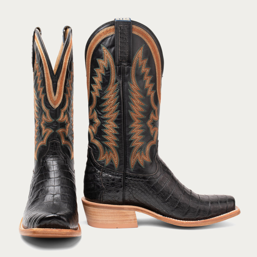 Pair of black cowboy boots with brown accents on a light gray background