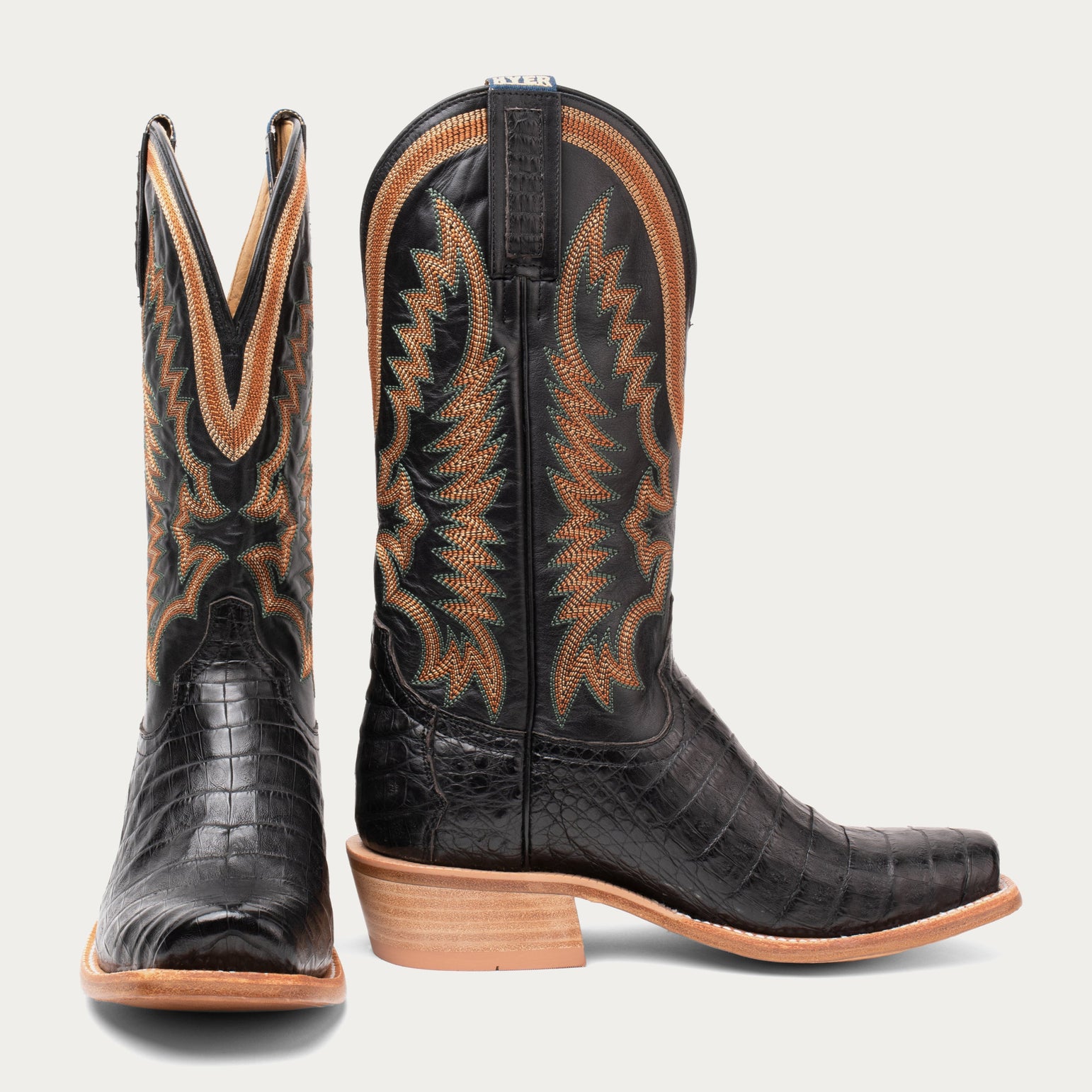 Pair of black cowboy boots with brown accents on a light gray background