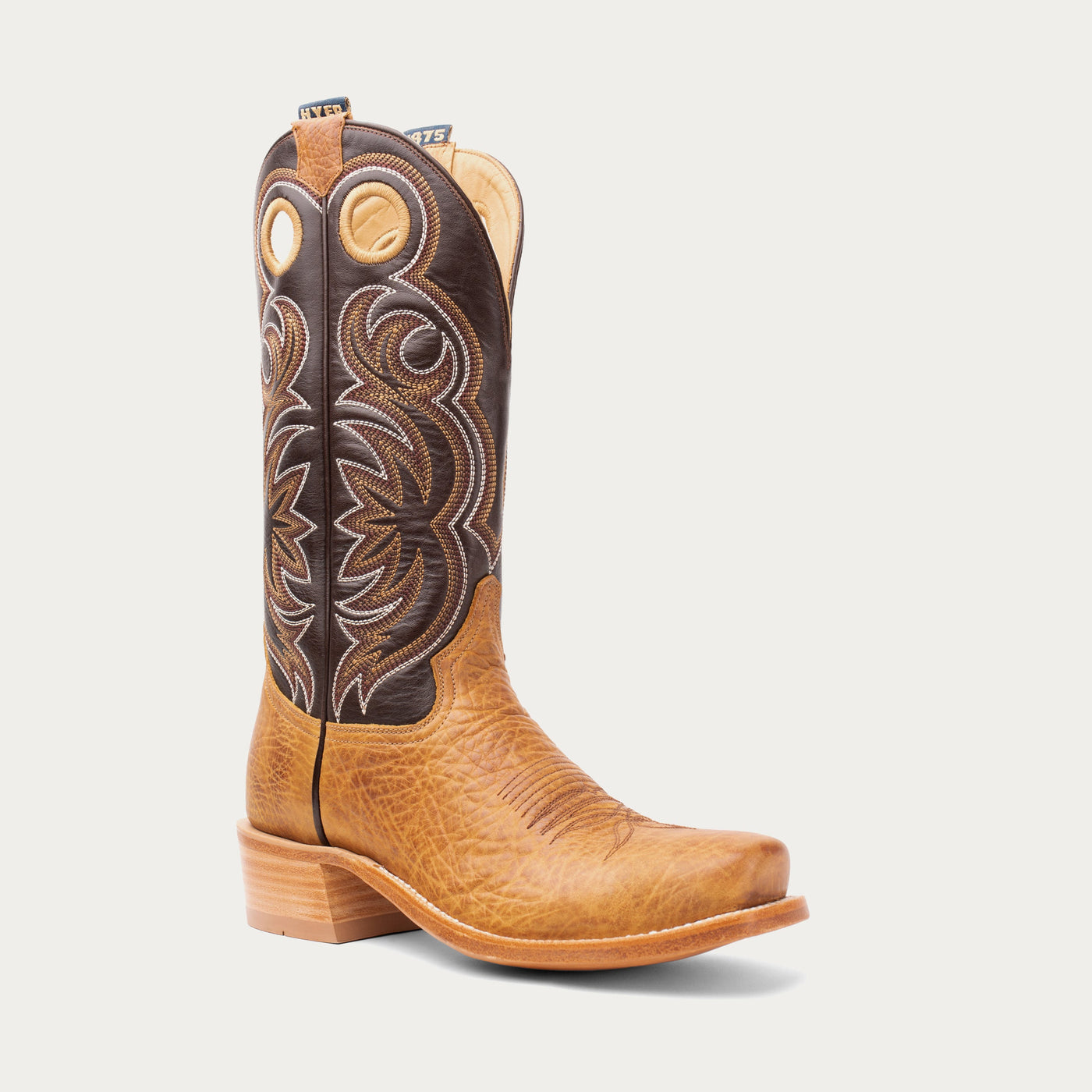 Light brown and dark brown cowboy boot with intricate stitching on a light gray background