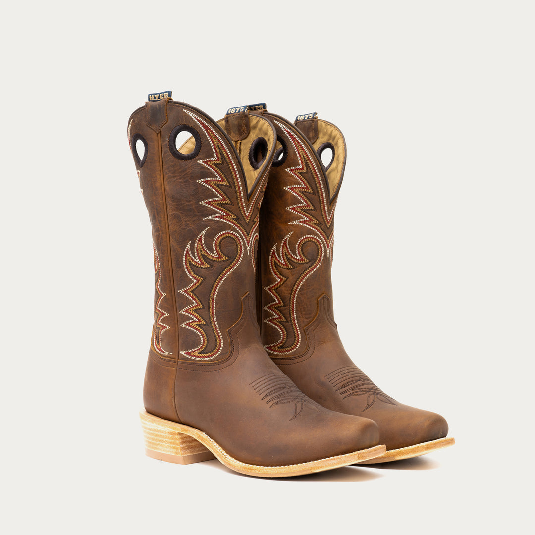 Pair of brown cowboy boots with intricate designs on a light gray background