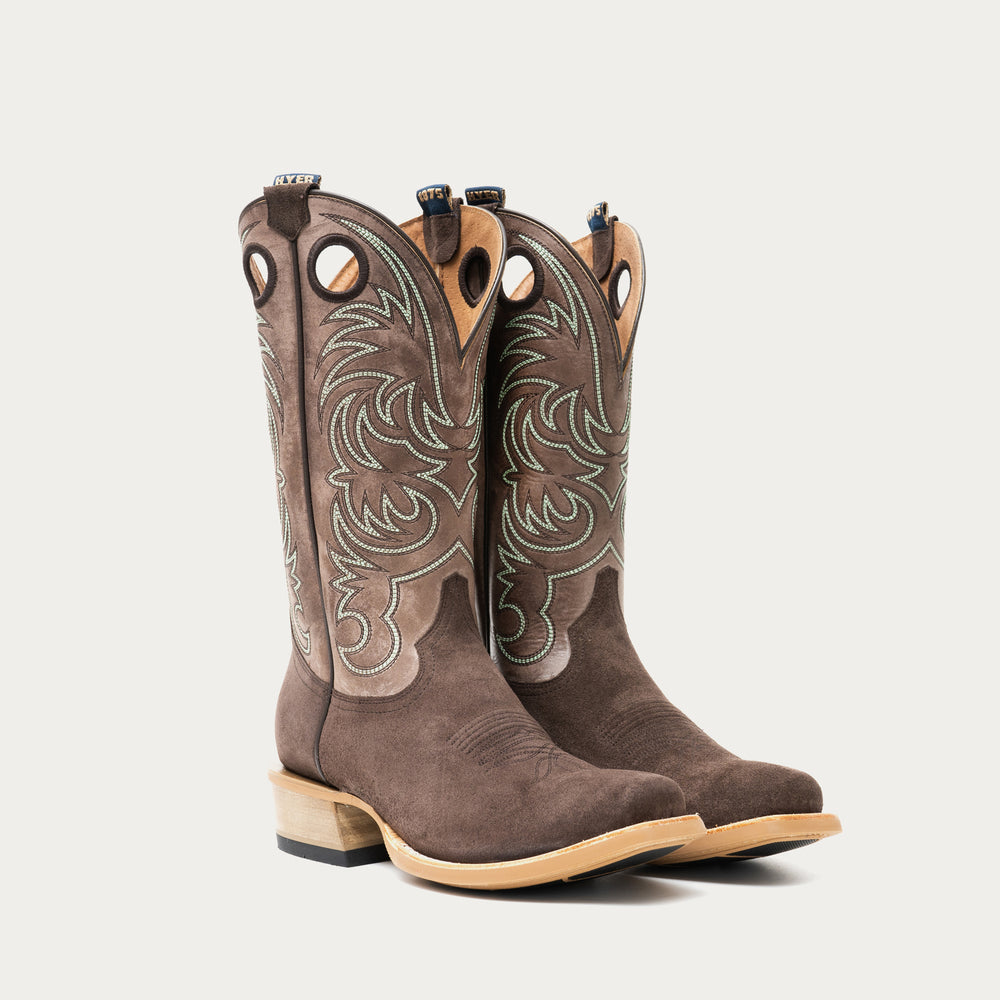 Pair of chocolate brown and taupe cowboy boots with brown and light blue intricate stitching on light gray background