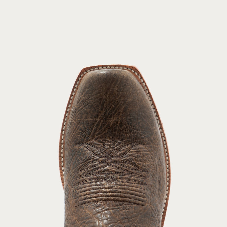 Close-up of the cutter toe of a distressed brown leather cowboy boot against a light gray background.