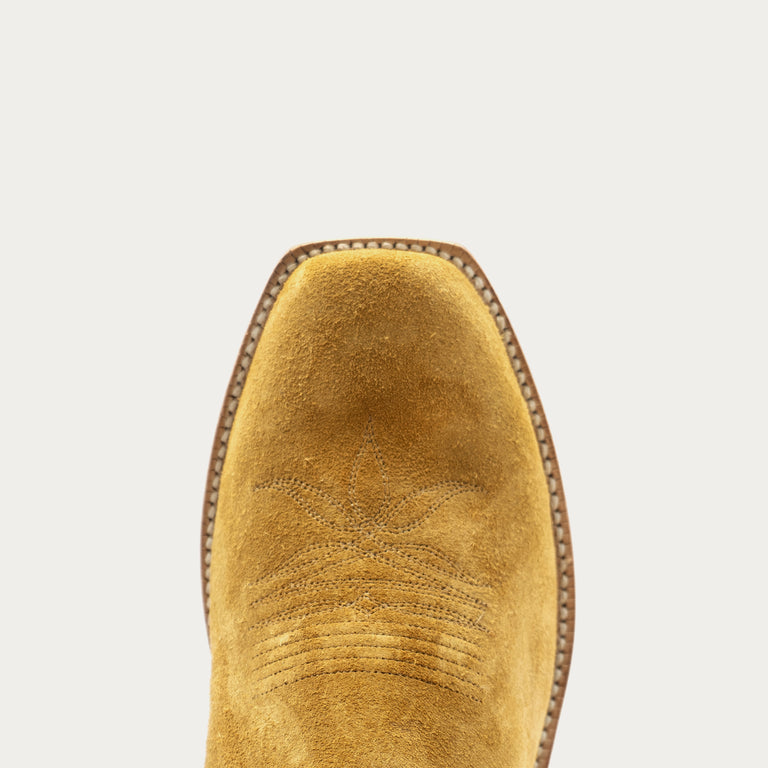 Close-up of the cutter toe of a tan rough out western boot on a light gray background.