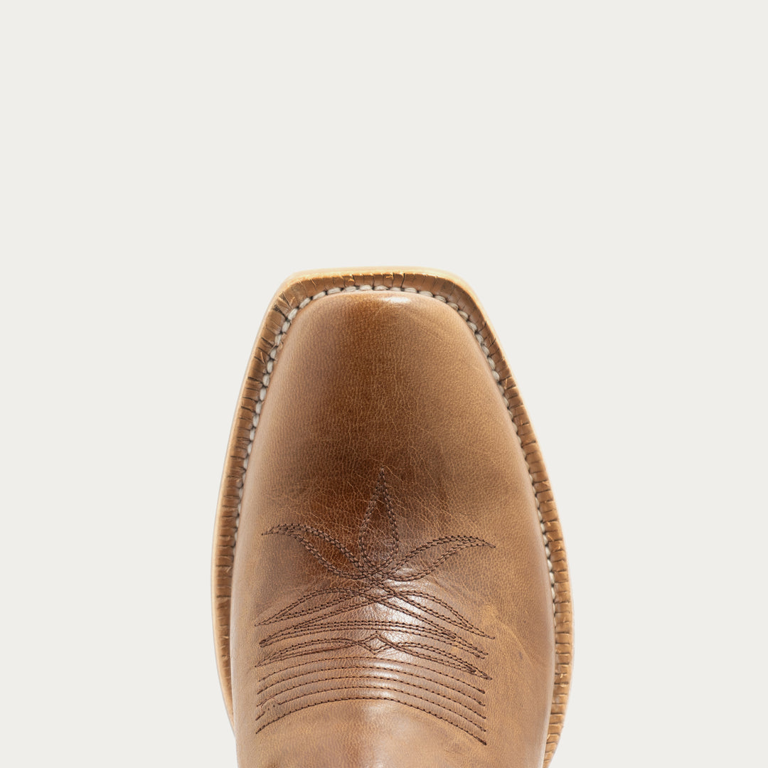 A close-up top-down view of a tan leather cowboy boot toe showing decorative stitching against a light gray background.
