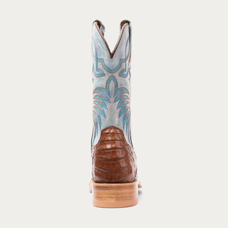 Cowboy boot with brown sole and blue patterned back on a light gray background