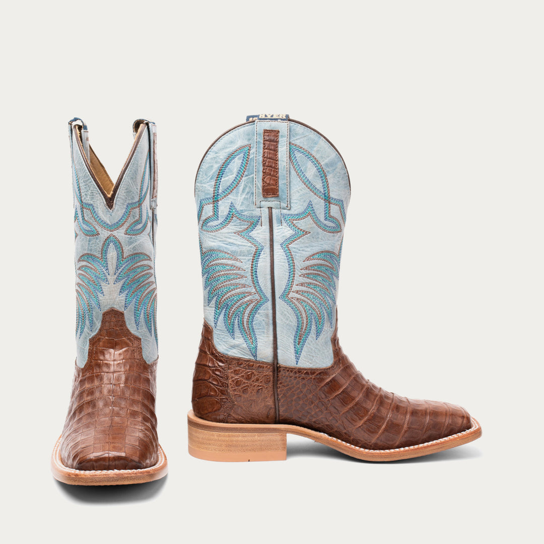 Pair of brown cowboy boots with blue and white pattern on a light gray background