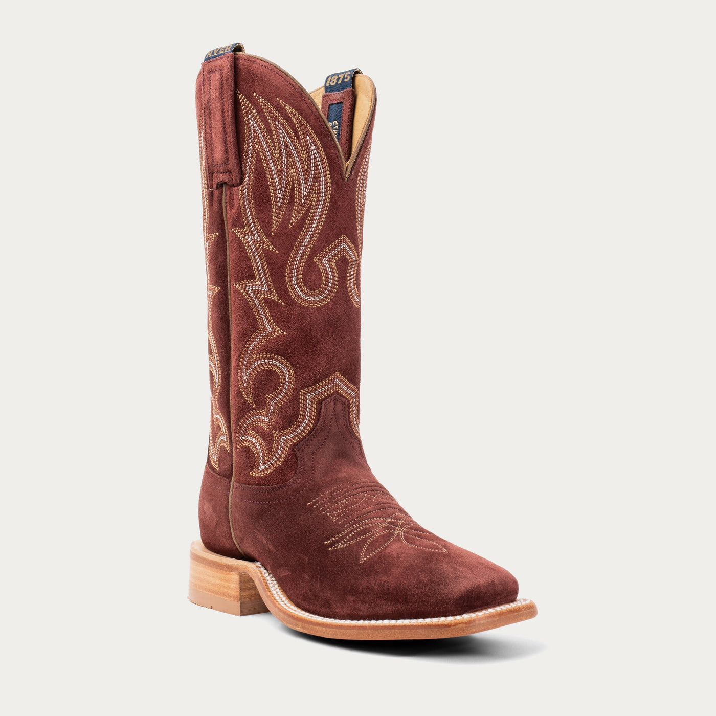 Burgundy red cowboy boot with intricate white and tan stitching on a light gray background