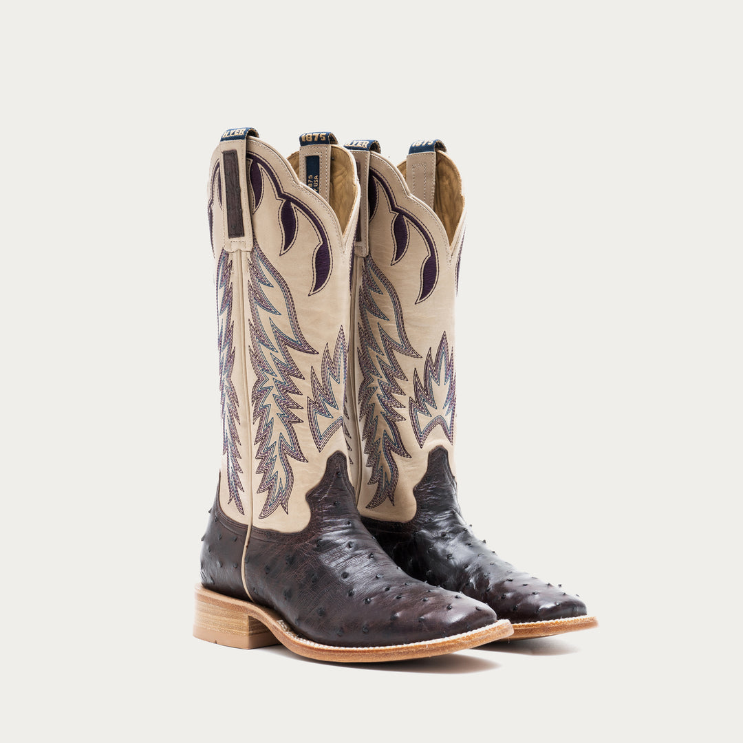 Pair of off white and dark purple cowboy boots with detailed design on a light gray background