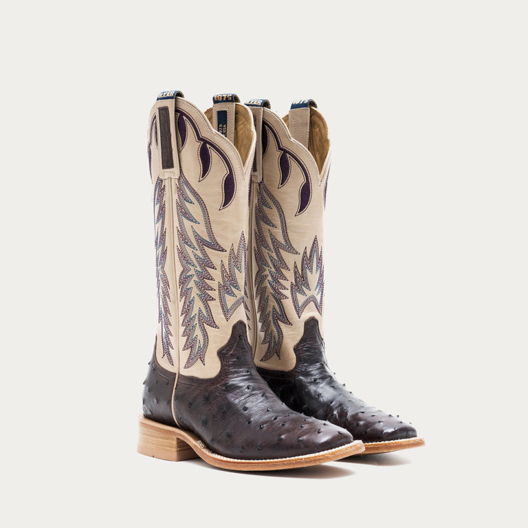 Pair of off white and dark purple cowboy boots with detailed design on a light gray background