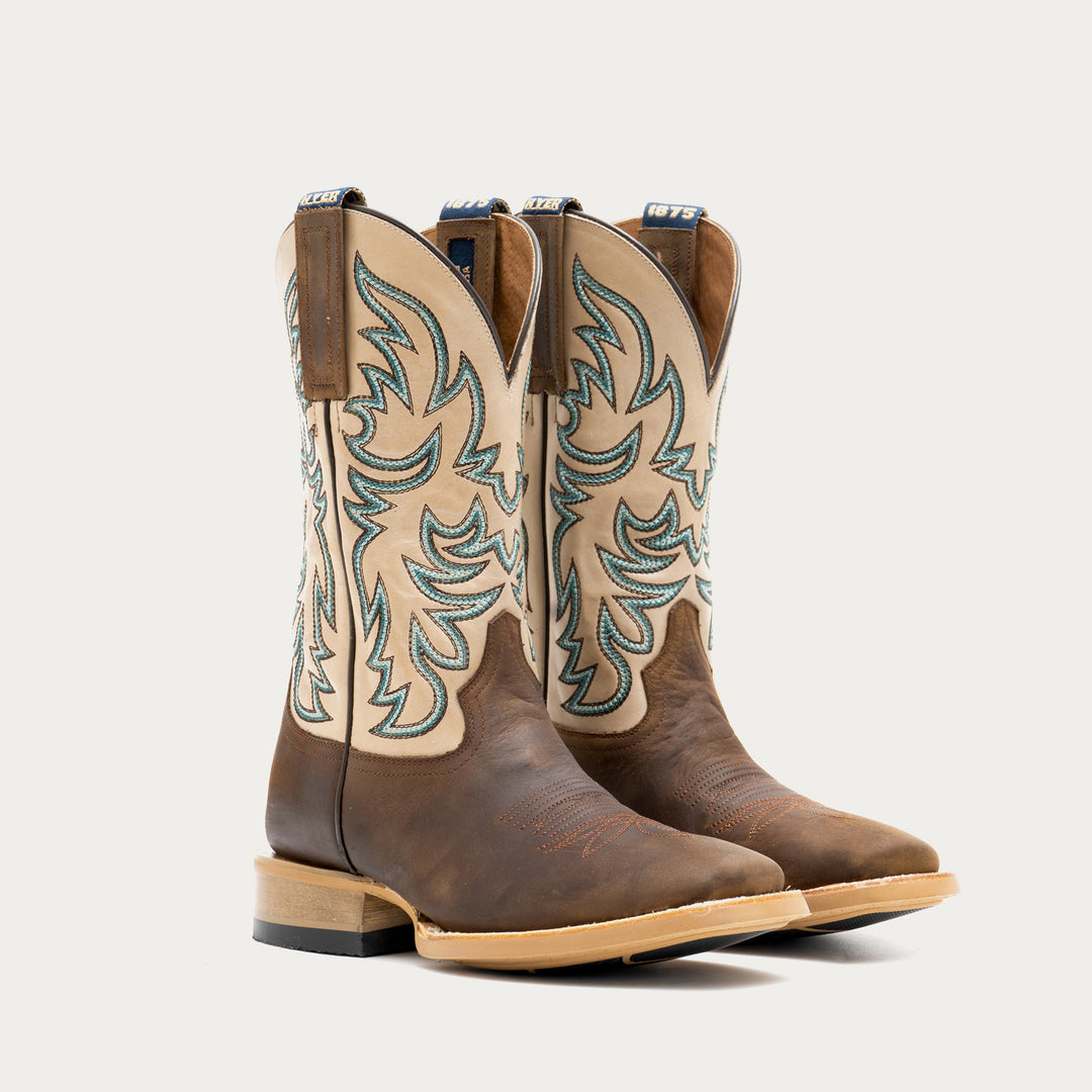Pair of brown and off white cowboy boot with intricate brown and blue embroidery on a light gray background